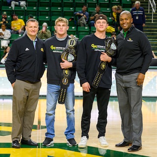 Two Mason wrestlers holding championship belts, flanked by their coaches